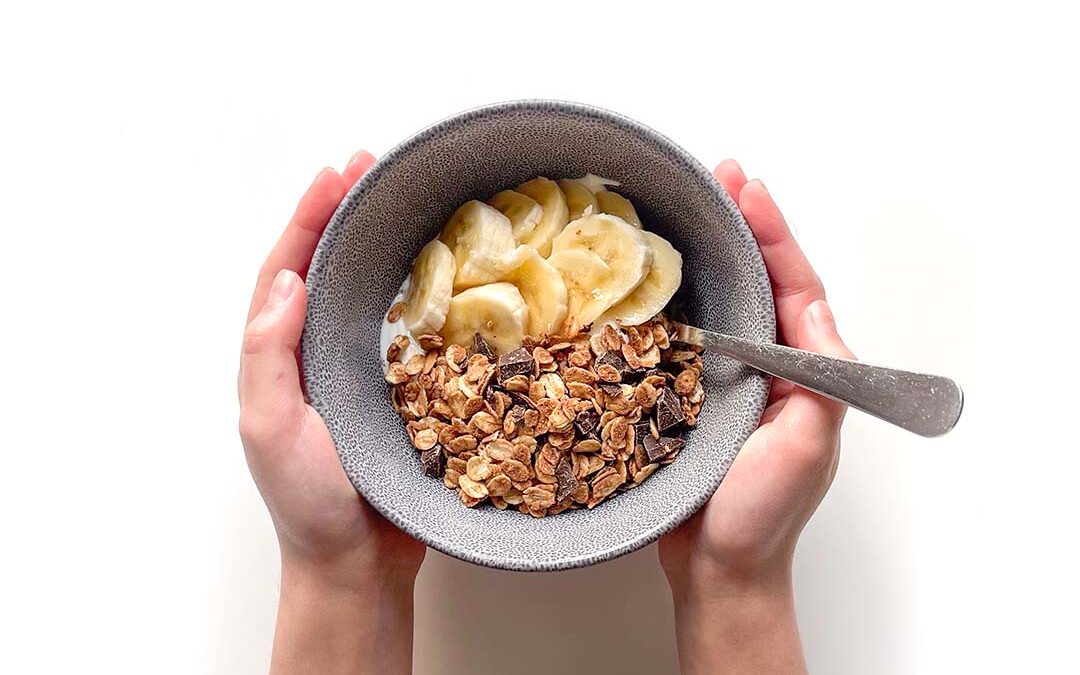 mãos segurando uma taça de iogurte com granola simples de chocolate